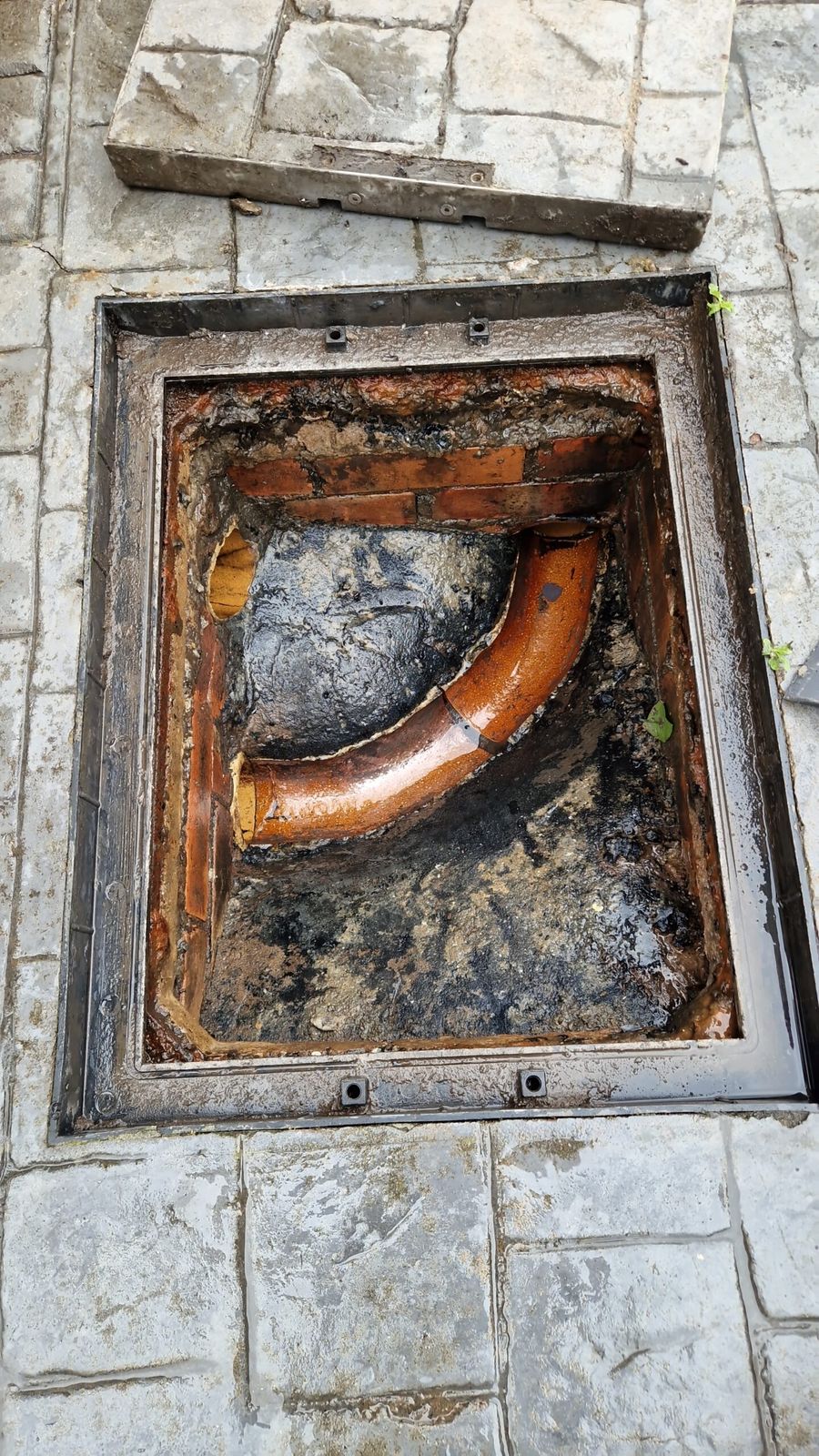 Open drain inspection chamber in a patio, showing the channel and debris