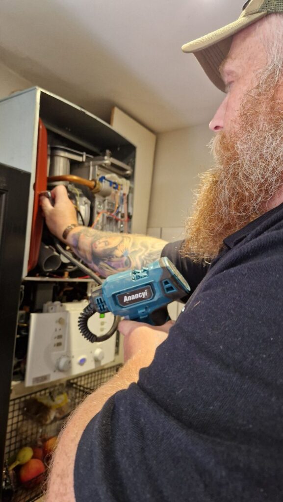 Engineer working inside an open gas boiler with a cordless tool