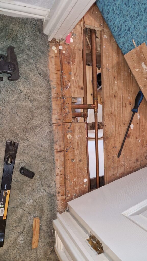 Floorboards lifted to reach copper pipework under the floor