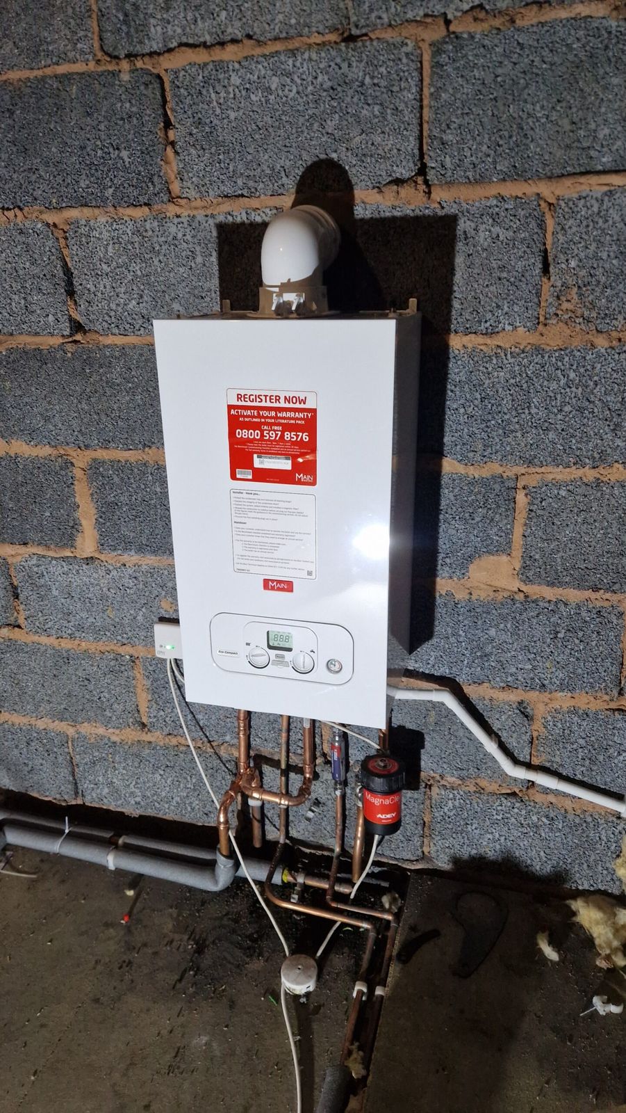 New white gas boiler fitted on a block wall, with copper pipework and controls below
